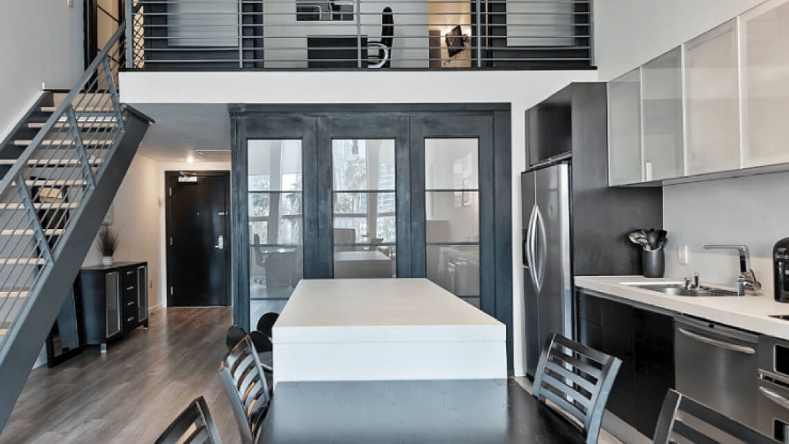 Modern loft kitchen with a central island, stainless steel appliances, and a staircase leading to an upper level.