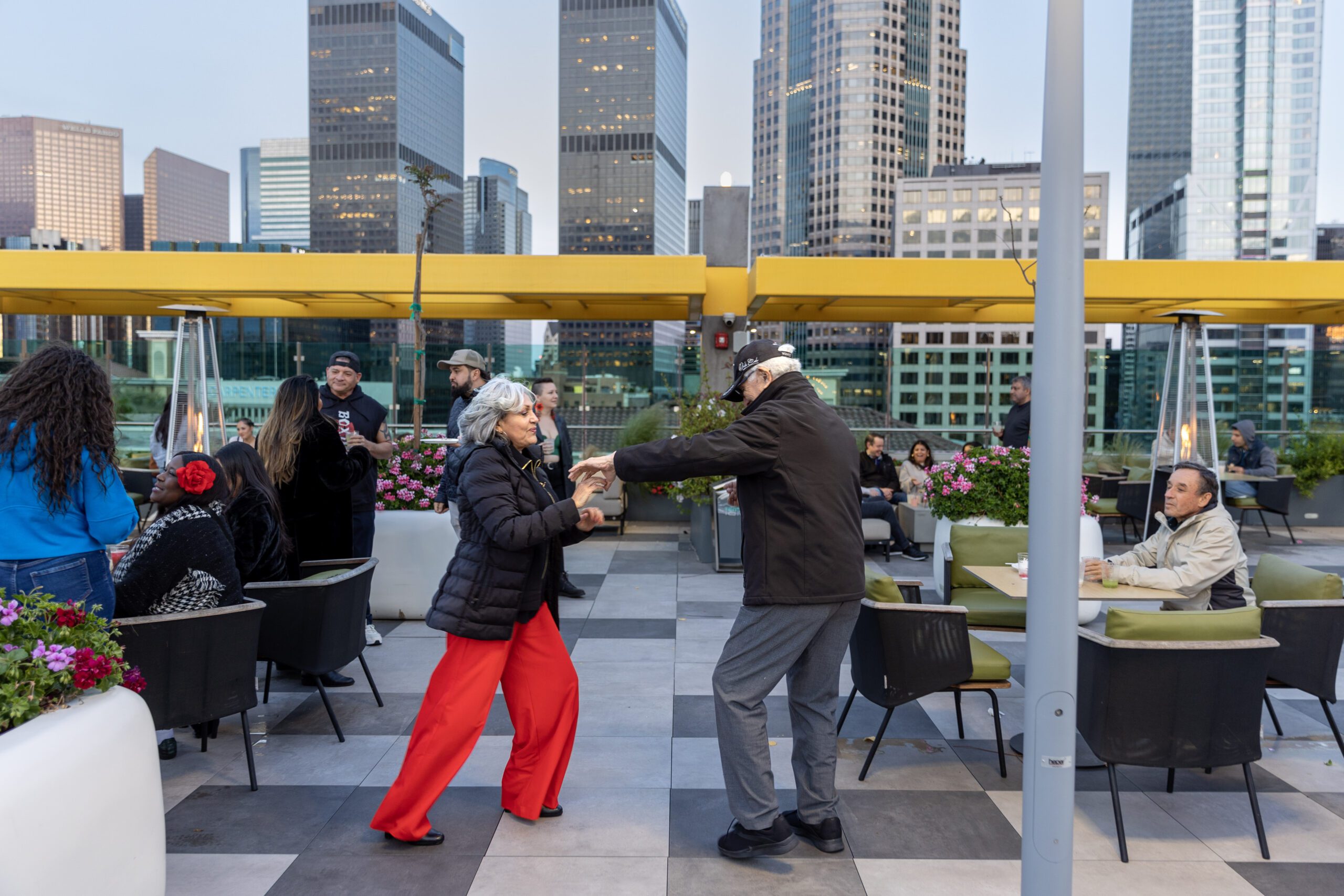 an elderly couple dancing joyfully on a rooftop terrace with a city skyline in the background