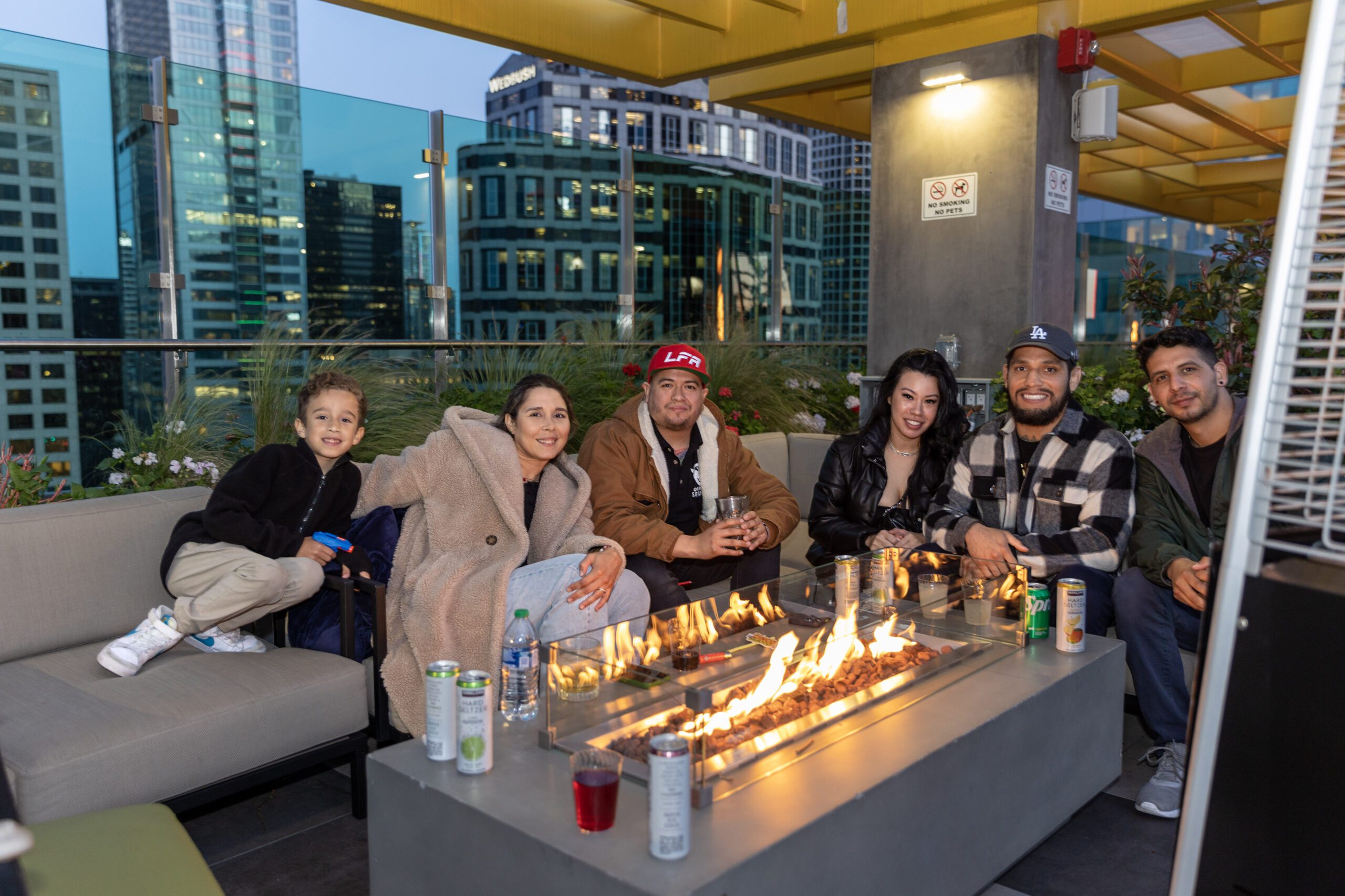 group of people enjoying drinks around a rooftop fire pit at night