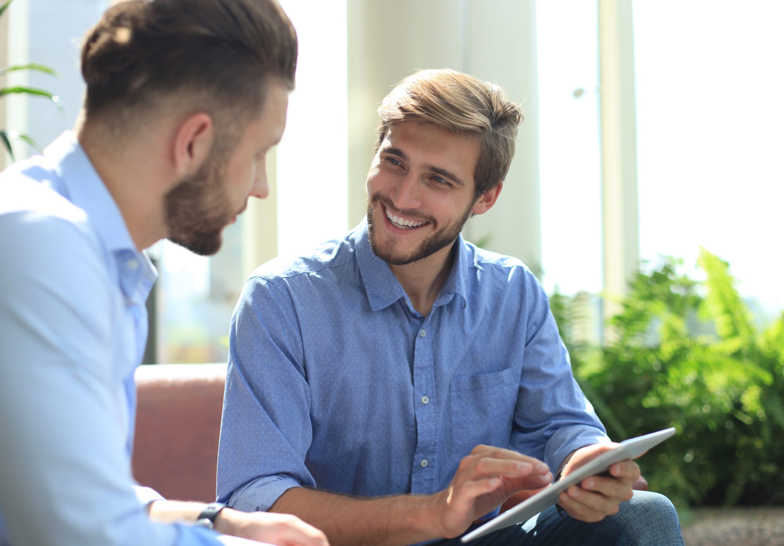 Mature businessman using a digital tablet to discuss information with a younger colleague in a modern business office.