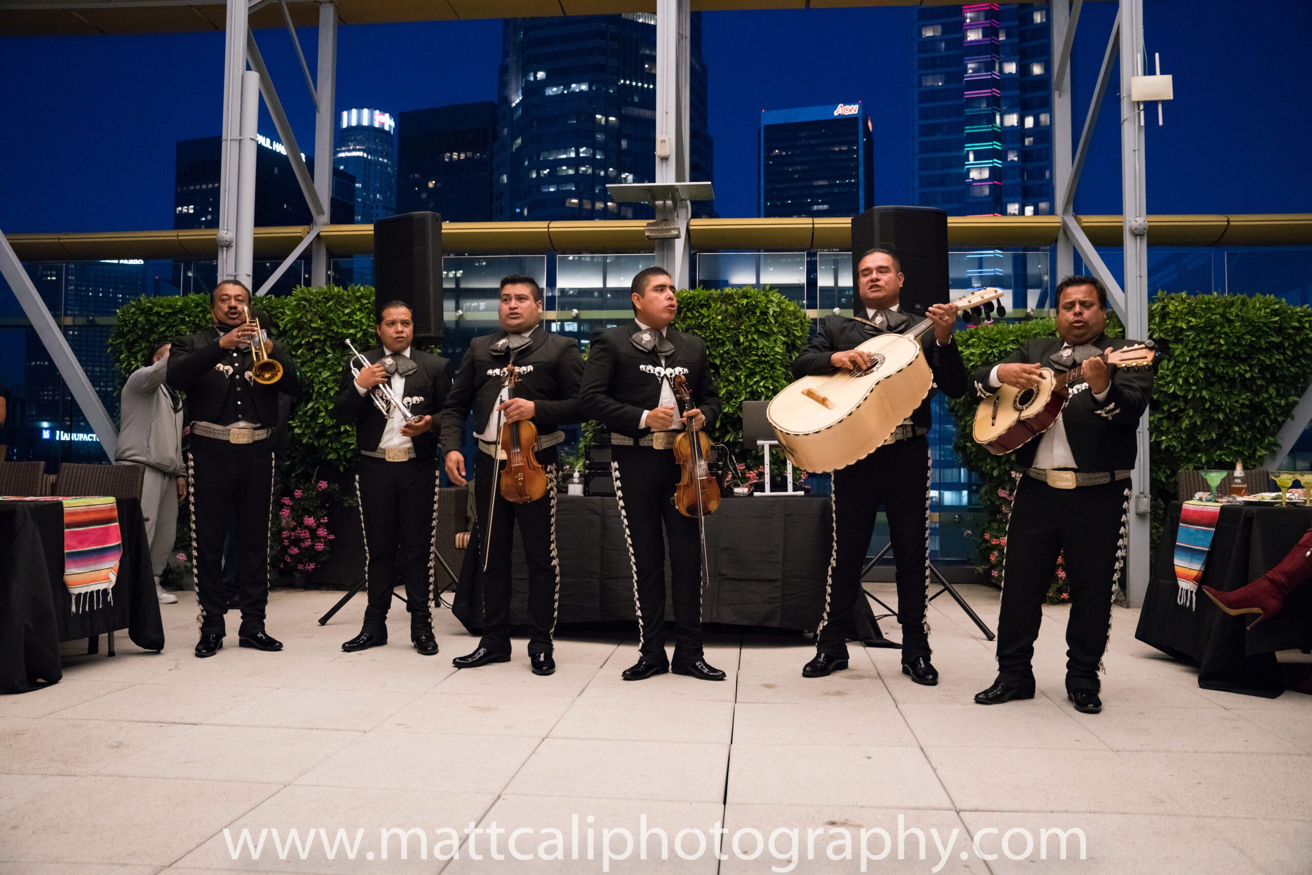 a mariachi band is performing on a rooftop at night with a city skyline in the background.