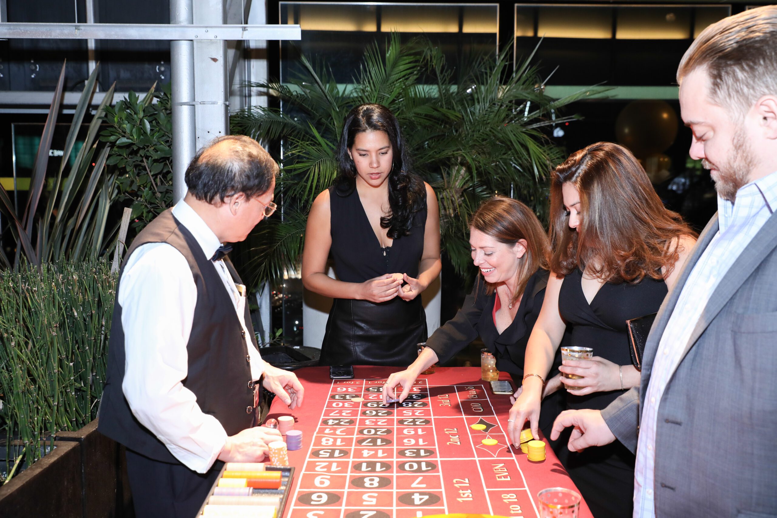 a group of people is gathered around a roulette table, engage in a casino-style game.